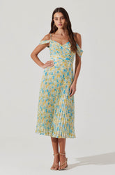 A woman is wearing a sleeveless, ankle-length dress with thin spaghetti straps and off-the-shoulder ruffle sleeves. The dress features a multicolored pattern in shades of yellow, blue, and white, with a fitted waist and a pleated skirt. She is also wearing strappy beige high-heeled sandals.